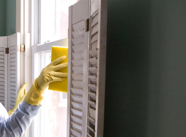 worker cleaning the windows of a green greyish house with white glass windows