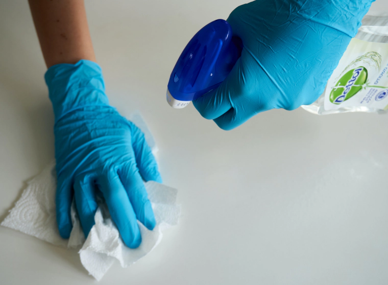 worker with blue gloves a paper towel and a cleaning solution cleaning a white surface